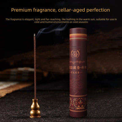 A cylindrical dark brown incense stick holder with gold decorative patterns stands next to a single lit incense stick resting in a small gold holder. The scene is set on a dark textured surface with a blurred dark background, featuring promotional text at the top.