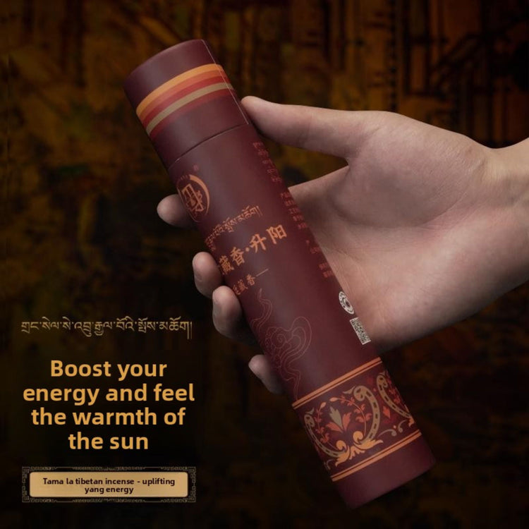A hand holding a cylindrical Tibetan incense holder wrapped in deep maroon paper with gold and orange decorative bands and text. The background is dark and atmospheric, with promotional text on the left in English and Tibetan script.